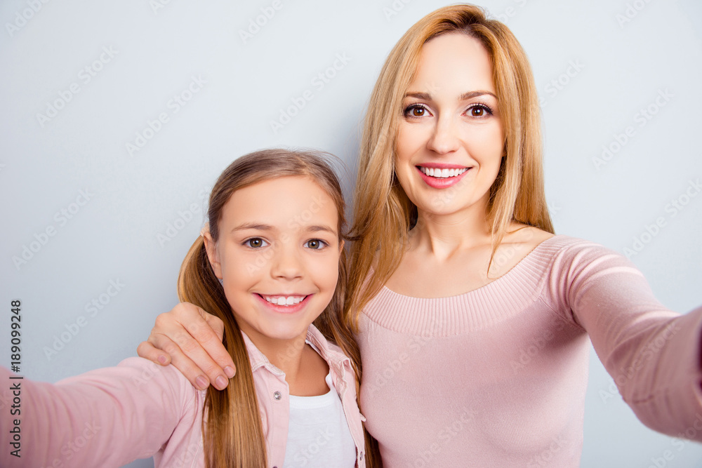 Smiling, nice, sweet, cute mother and daughter with beaming smiles, making selfie together on smart phone, front camera over gray background Smiling, nice, sweet, cute mother and daughter with beaming smiles, making selfie together on smart phone, front camera over gray background