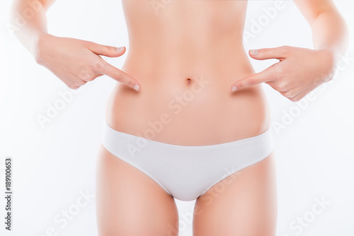 Menstruation ovulation depilation epilation laser liposuction sport weight loss concept. Cropped close up photo of skinny woman's ideal belly demonstrating with fingers isolated on white background © deagreez