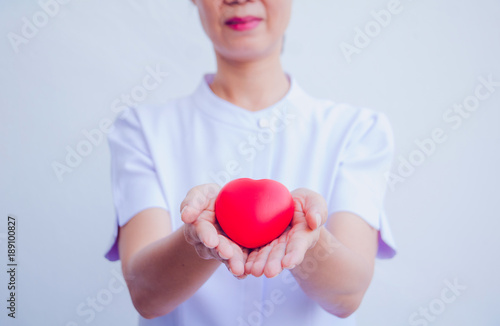 Fototapeta Naklejka Na Ścianę i Meble -  A nurse holding red heart toy. She is Left / right hand holding it. She is smile and good mood. The photo shows the principle of caring and good health.