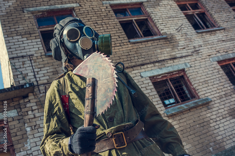 Soldier in old tactical gear with gas mask and with DIY sharp axe in post- apocalyptic abandoned city Stock Photo