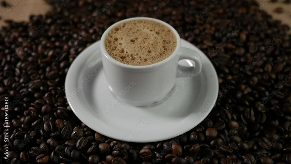Coffee cup and coffee beans. A white cup of evaporating coffee foam on a table with fried beans. Coffee cup and coffee beans. A white cup of evaporating coffee foam on a table with fried beans.