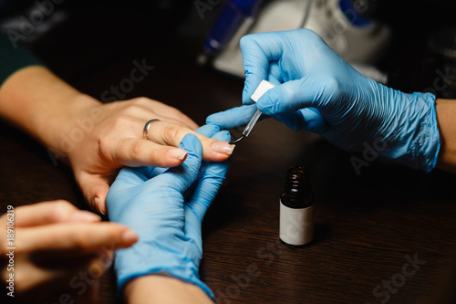 A professional manicurist puts color gel nail Polish brush on the finger of the client after applying the shellac. A close up shot of hardware manicure at the beauty salon.