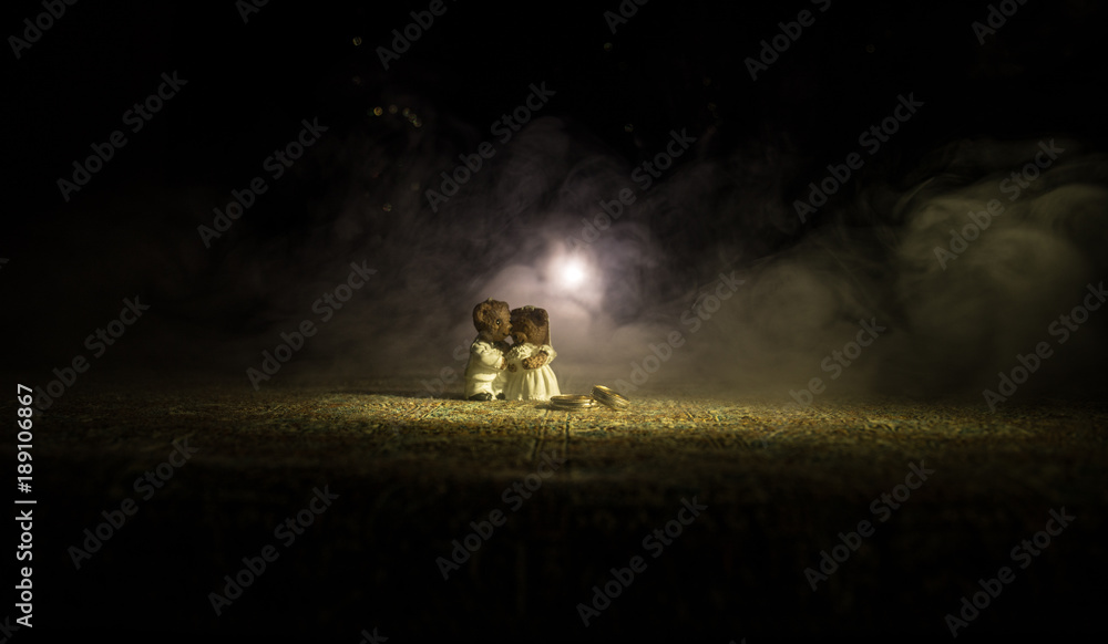 Fototapeta premium Stuffed bride and groom bears standing together with LED heart on dark foggy background.