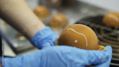 Process of creating delicious dessserts. Unrecognizable confectioners hands in blue gloves take cakes off tray and decorate with crisps. Close-up footage photo