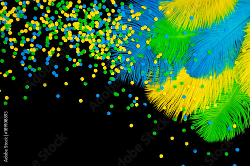 Poultry feathers and confetti are green, yellow and blue. Black background. Feathers for the Brazilian carnival costume. photo
