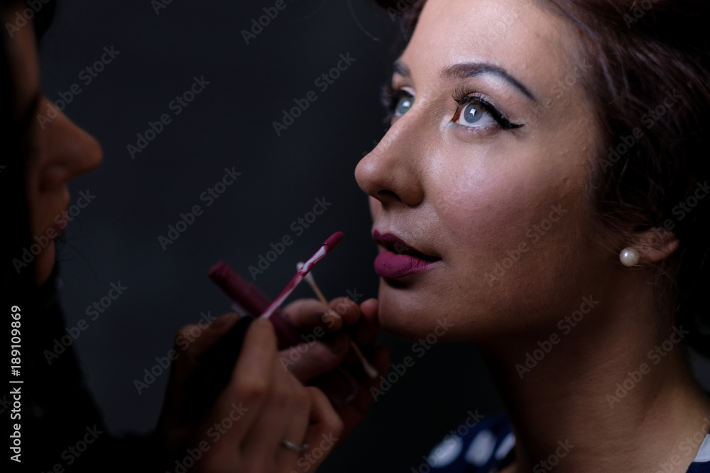 Fototapeta premium Makeup artist applies lips a red lipstick. Beautiful woman face. Perfect makeup on retro pinup or vintage pin up style