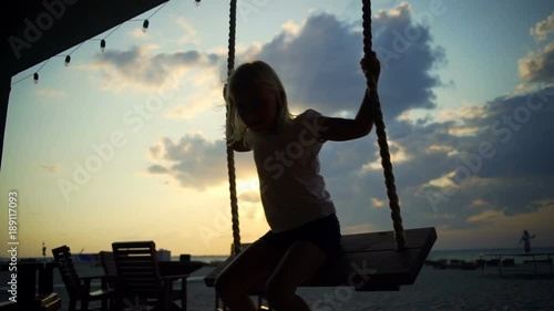 Blonde baby girl seating on teeter at sunset rapid slow mothion photo