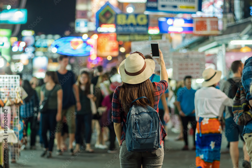 Back side of Young Asian traveling women taking photo in Khaosan Road walking street at night in Bangkok, Thailand, traveler and tourist concept Back side of Young Asian traveling women taking photo in Khaosan Road walking street at night in Bangkok, Thailand, traveler and tourist concept