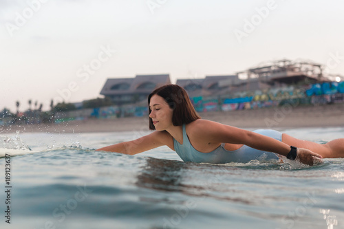 Photography Young woman in bright bikini surfing on a board in ocean