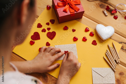 The girl wrote a letter with congratulations and pastes the envelope with a symbol in the form of a heart. Nearby lie various objects symbolizing the event.