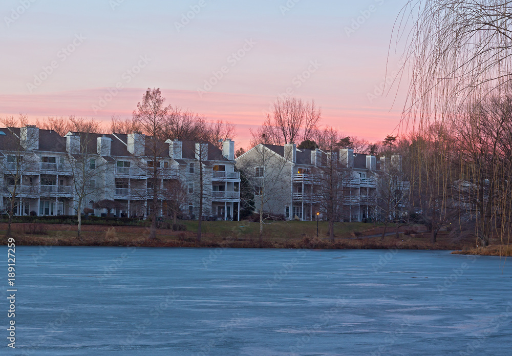 Colorful sunset in residential neighborhood near lake covered in ice. Pastel colors of winter sunset at lake waterfront in Falls Church, Virginia, USA.