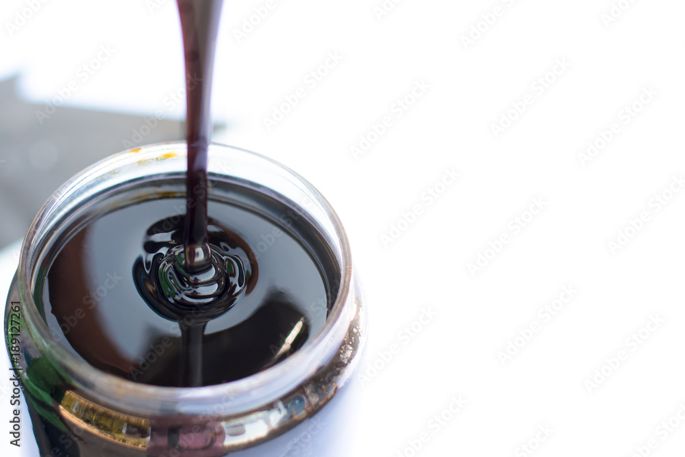 Molasses sugarcane on glass isolate on white background. Droping molasses with hands. Molasses