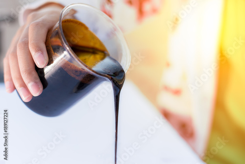 Molasses sugarcane on beaker. Droping molasses with hands. Molasses is the final product from the sugarcane extraction process of sugar factory. industrial concepts.