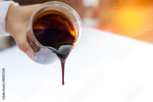 Molasses sugarcane on beaker. Droping molasses with hands. Molasses is the final product from the sugarcane extraction process of sugar factory. industrial concepts.