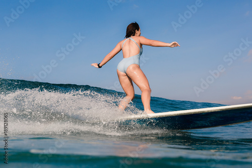 Photography Young woman in bright bikini surfing on a board in ocean