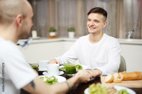 Two young gay men holding by hands during breakfast and talking