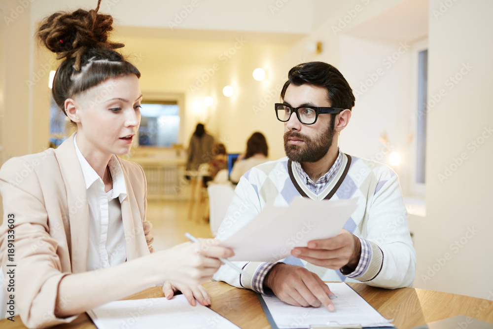 Fototapeta premium Serious employee showing paper or contract to his colleague during work in cafe
