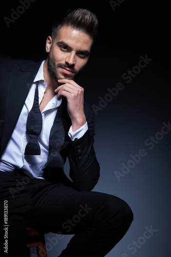 man in tuxedo with untied bowtie is smiling and thinking photo