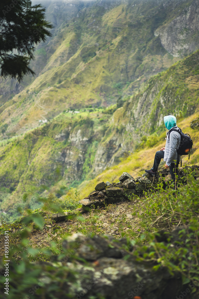 Tourist with backpack looking over the rural landscape with mountain ridge on the path to the Xo-Xo Valley. Santo Antao Island, Cape Verde