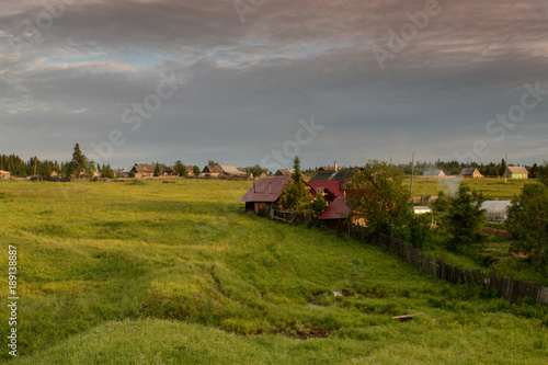 a typical Russian village  wooden houses  the smoke from the chimney  blue sky  green fields