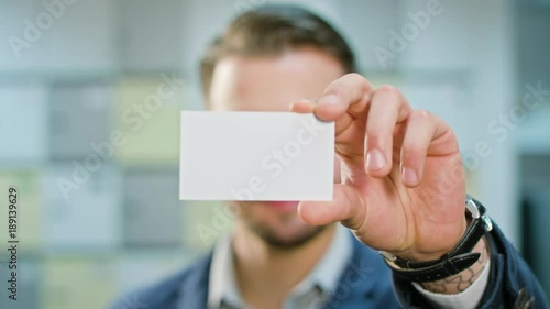 A handsome smiling businessman showing a blank piece of paper. Close-up shot. Soft focus.