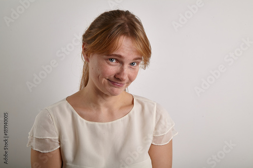 Closeup shot of young girl with ginger hair dressed in casual creamy white blouse looking at the camera with "shame on you" expression, pointing out somebody's mistake