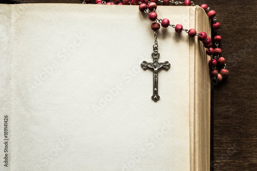 Foto Opened old thick bible with rosary beads on the brown table in the quiet, dark atmosphere