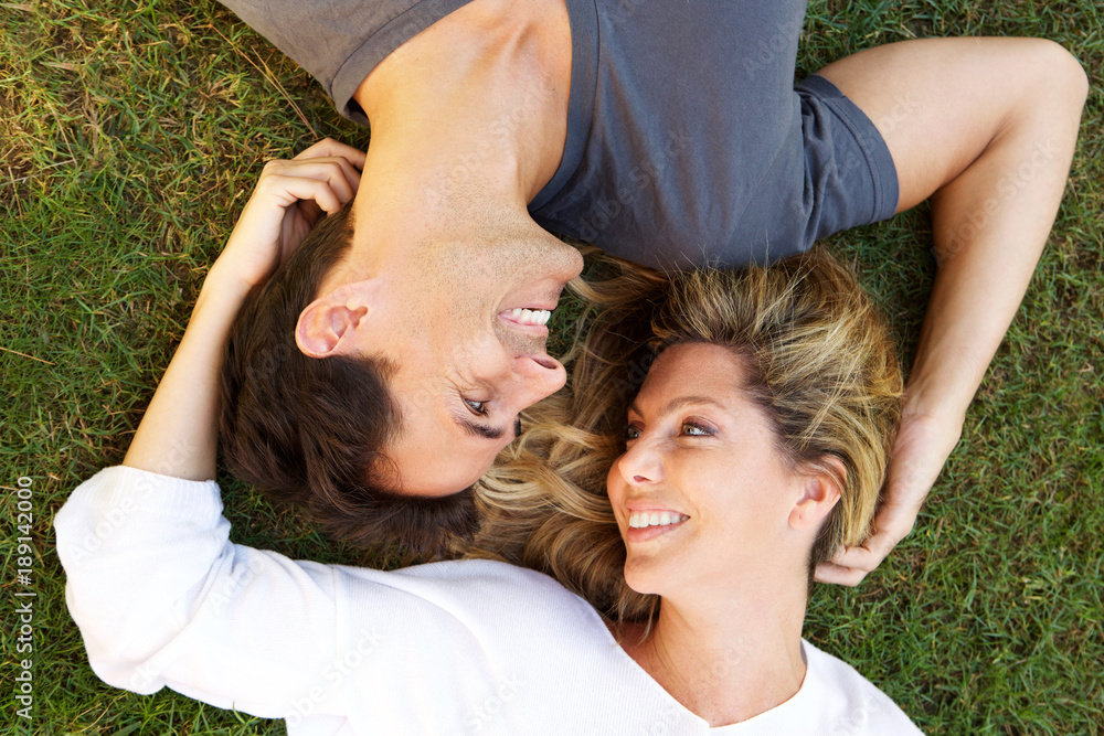 Close up carefree couple lying on grass together in love Close up carefree couple lying on grass together in love