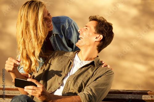 happy boyfriend and girlfriend laughing together outside with mobile phone