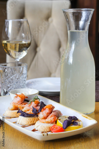 Baked shrimps in bacon on bruschettes with a glass of white wine and morsel - restaurant serve