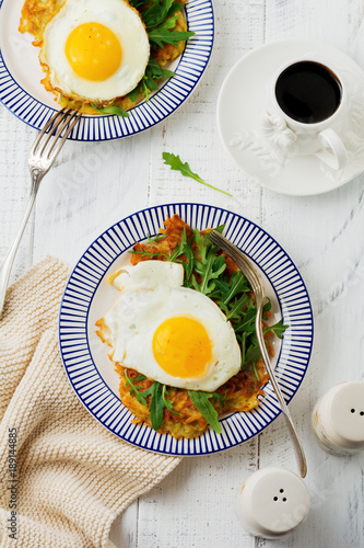 Fried egg with potato pancake, arugula and avocado on ceramic plate for breakfast on white wooden table background. Selective focus. Top view. Copy space.
