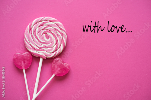 Pink Valentine's day heart shape lollipop candy on empty pink paper background. With Love greetng card.