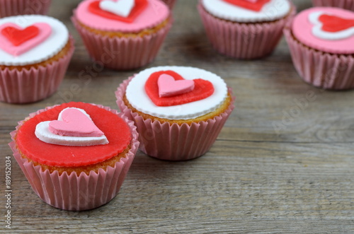 CUPCAKES decorated with hearts arranged on wooden background