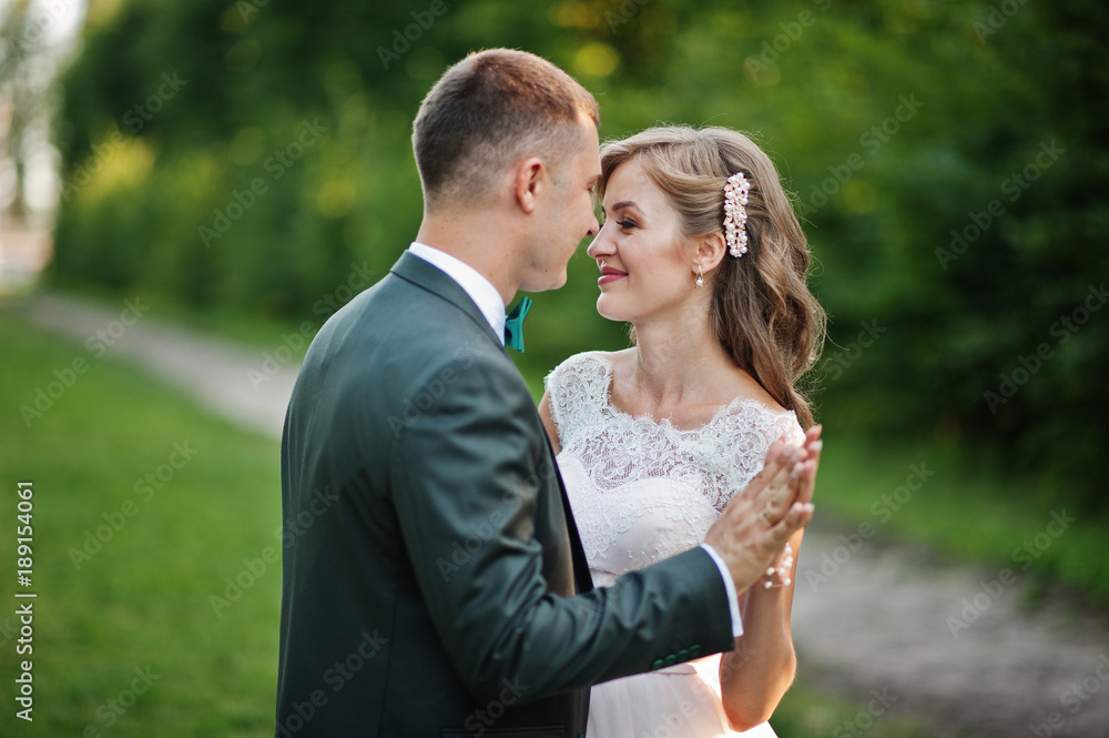 Lovely wedding couple walking along the green alley which leads to a church.