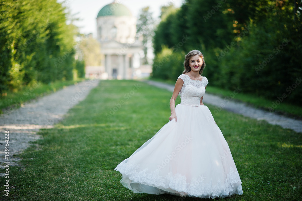 Lonely attractive bride walking on the green alley which leads to a church.
