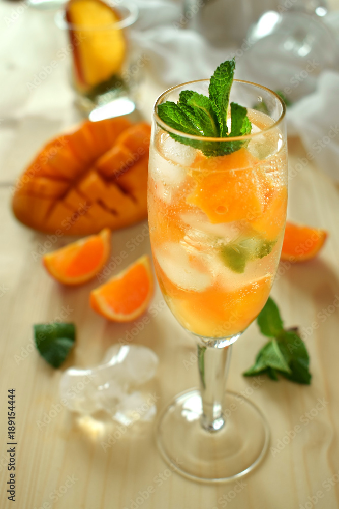 Sparkling cocktail with mango pieces, ice cubes and mint in a wineglass Sparkling cocktail with mango pieces, ice cubes and mint in a wineglass