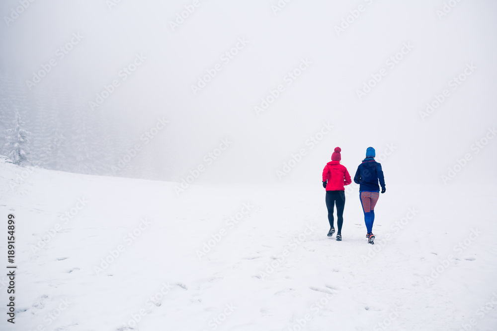 Two women trail running on snow in winter mountains