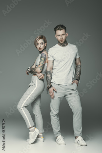 fashionable tattooed couple in sportswear posing together, isolated on grey