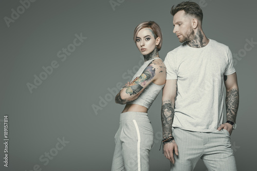 Fotografia stylish tattooed couple in sportswear posing together, isolated on grey