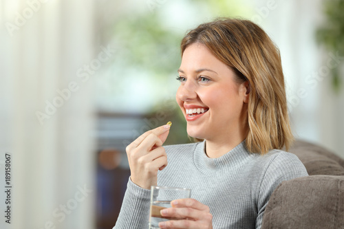 Fotografia Happy blonde girl taking a vitamin pill at home