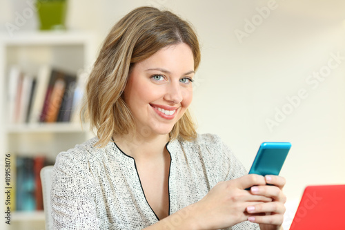 Satisfied girl holding a smart phone looking at you