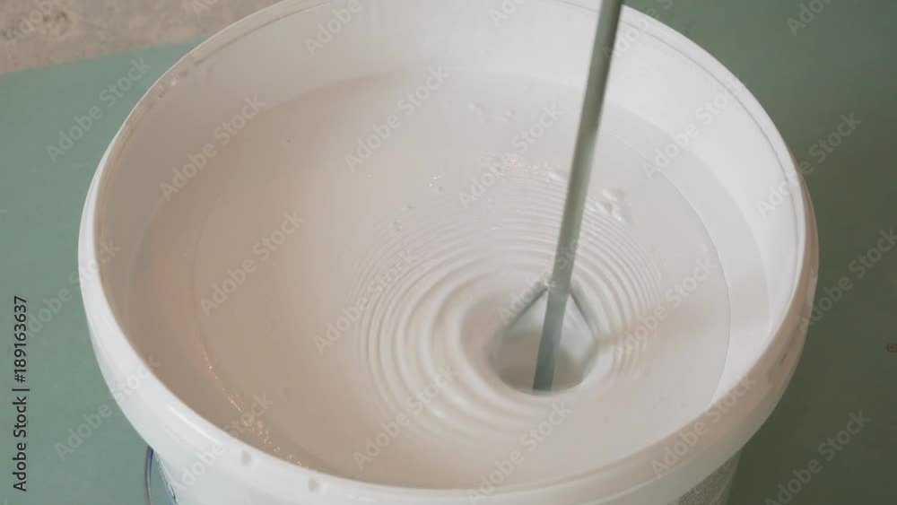 The process of mixing white paint by the drill in the bucket The process of mixing white paint by the drill in the bucket