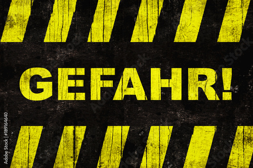 Gefahr (in German, “danger”) text warning sign with yellow and black stripes painted over grungy cracked wood.