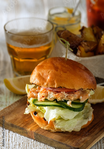 Fishburger with toppings, fries and a glass of beer. Rustic style