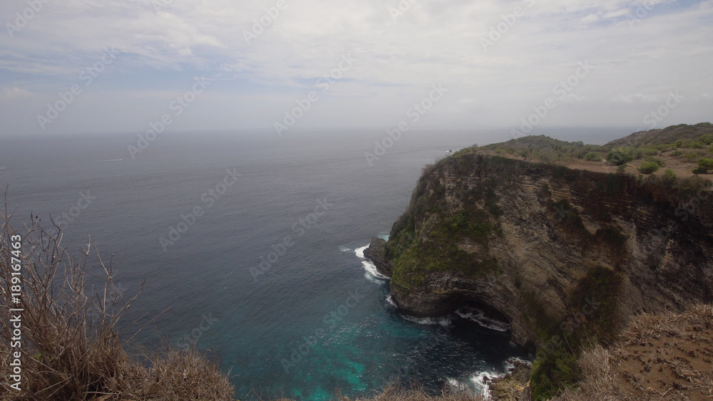 Cliff with waves crashing against rocky shore, Nusa Penida, Indonesia. Rocky coast and ocean with waves and rocky cliff. Travel concept.