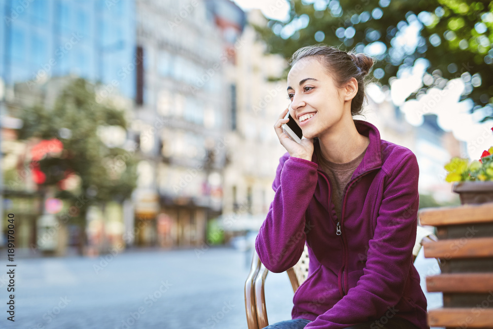a young smiling woman tourist in sportswear seets on the bench in the center of Prague with a phone in the hands of. travel guide, tourism in Europe, woman tourist with smartphone on the street a young smiling woman tourist in sportswear seets on the bench in the center of Prague with a phone in the hands of. travel guide, tourism in Europe, woman tourist with smartphone on the street