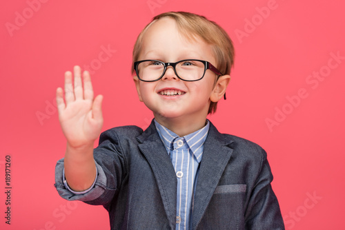 portrait of smiling little boy in eyeglasses isolated on pink