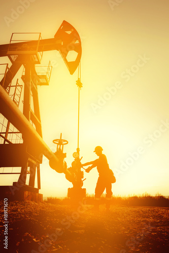 Oil worker is checking the oil pump on the sunset background.