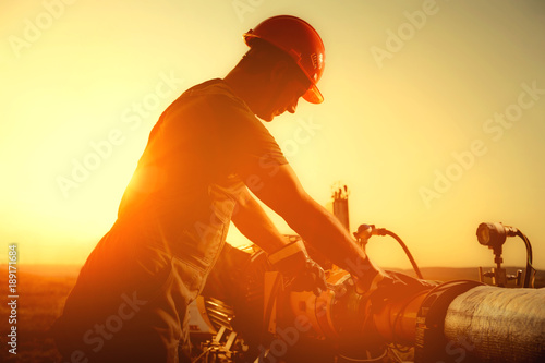 Oil worker is checking the oil pump on the sunset background.