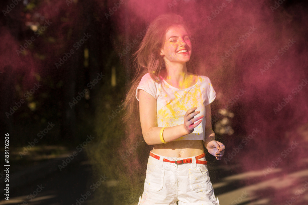 Obraz premium Lovely brunette model having fun in a cloud of yellow and pink dry paint at Holi festival
